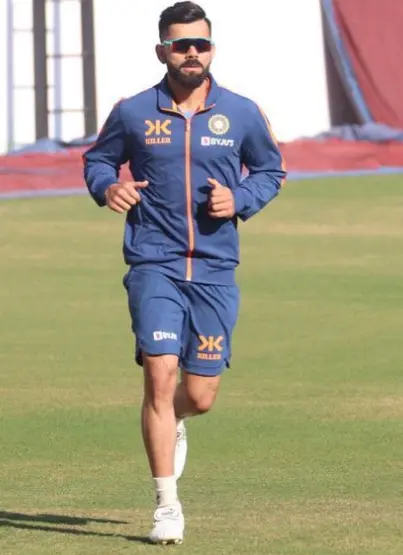 "Virat Kohli standing on the cricket field, showcasing his athletic build and height."

