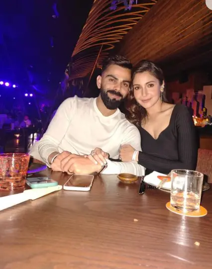 "Virat Kohli with his girlfriend, enjoying a quiet evening together, smiling and looking happy."

