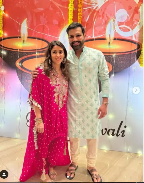 "A candid photo of Rohit Sharma and his wife, Ritika Sajdeh, smiling together during a public event. Ritika looks elegant in a traditional Indian outfit, while Rohit sports a casual yet stylish look."